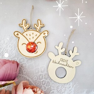 May include: Two wooden Christmas ornaments shaped like reindeer heads. One ornament has a red candy cane in the center of the reindeer's face. The other ornament has the text "Frohe Weihnachten" written on it.