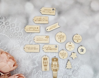 May include: A collection of wooden Christmas ornaments with various festive designs and phrases, including "Frohe Weihnachten", "Frohes Fest", "Stille Nacht", and "Hallo Winter".