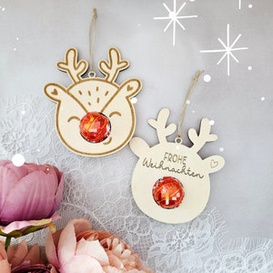 May include: Two wooden reindeer ornaments with red and gold candy inside. The reindeer on the left has a red nose and the reindeer on the right says "Frohe Weihnachten" in German.