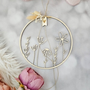 Puede incluir: Un aro de madera con un diseño floral, que incluye una pequeña etiqueta en forma de corazón con la palabra "love" en ella. El aro está decorado con flores secas y una cuerda de yute.