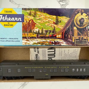 Può includere: Set di modellini di treni Athearn in una scatola. La scatola presenta un'illustrazione colorata di un treno e di un paesaggio montano. Il vagone del treno modello è verde scuro con la scritta "SOUTHERN PACIFIC LINES" stampata sul lato.