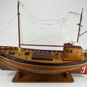 May include: A detailed wooden model of a fishing boat. The boat has a brown hull with black trim and a wooden deck. It features masts, rigging, and a small cabin. The model is mounted on a wooden stand, with the name "THOMAS RUTH" visible on the bow.