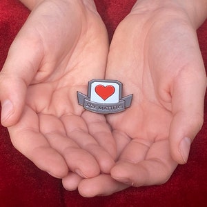 May include: A silver enamel pin with a red heart and the text "SIZE MATTERS" on a white banner.