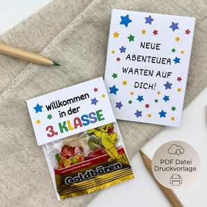 Könnte beinhalten: Zwei Karten und eine Süßigkeitentüte mit Text und Sternverzierungen. Auf einer Karte steht "NEUE ABENTEUER WARTEN AUF DICH!" und auf der anderen "Willkommen in der 3. KLASSE". Die Süßigkeitentüte hat eine gelbe Bärengrafik und die Worte "Goldbären".