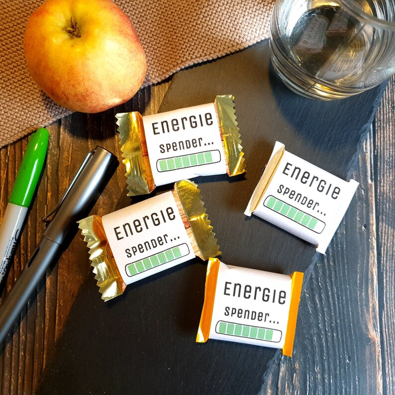 May include: Four small, gold-wrapped chocolate bars with a white label that reads "Energie Spender..." and a green progress bar. The bars are on a black surface.