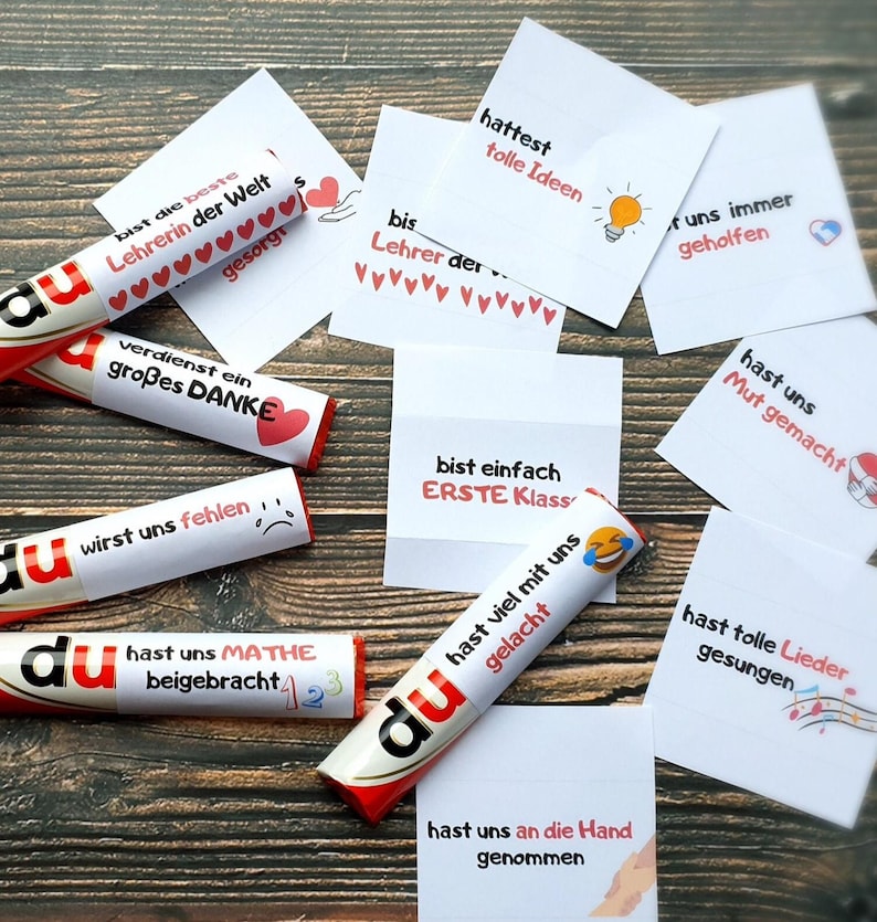May include: A collection of white paper labels and candy bars wrapped in white paper, each featuring German text and small colorful icons. The labels include phrases like bist die beste Lehrerin der Welt, hattest tolle Ideen, and hast uns Mathe beigebracht.