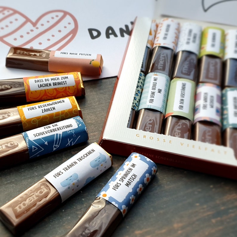 May include: A box of assorted chocolate bars with colorful wrappers featuring different messages. The messages include "For nose blowing", "For the rainworms counting", "For school preparation", "For drying tears", and "For jumping in the mud".