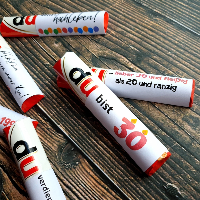 May include: Four red and white wrapped chocolate bars with different messages. The messages are "du hochleben!" "du bist 30" "du verdien" and "flei&szlig;ig im immer Kind".