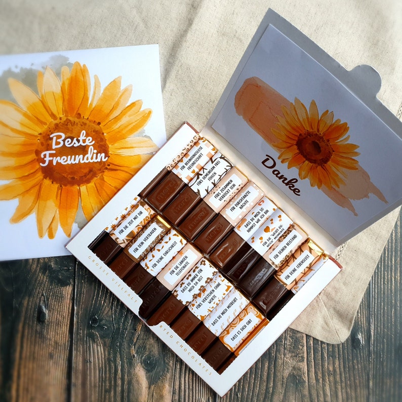 May include: A box of assorted chocolate bars with a sunflower design and the text "Beste Freundin" on the front. The chocolate bars are wrapped in gold foil and have different messages printed on them, such as "For the summer" and "For the laughter".