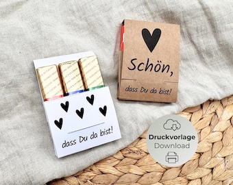 May include: Two small gift boxes, one white and one brown, with chocolate bars inside. The white box has black heart designs and the text "dass Du da bist!". The brown box has a black heart and the text "Schön, dass Du da bist!".