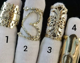 May include: Four gold-toned finger rings with different designs. The rings are displayed on a white fabric background. The rings are numbered 1 through 4.