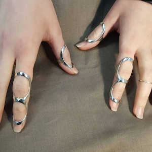 May include: Silver rings designed to fit on multiple fingers. The rings are open and have a curved shape.