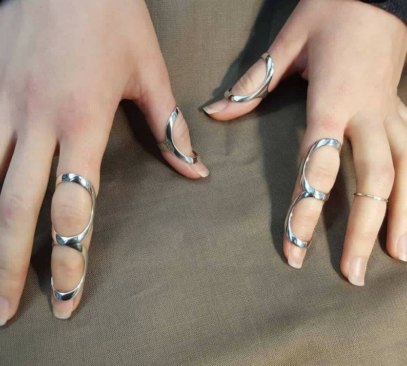 May include: Silver rings designed to fit on multiple fingers. The rings are open and have a curved shape.