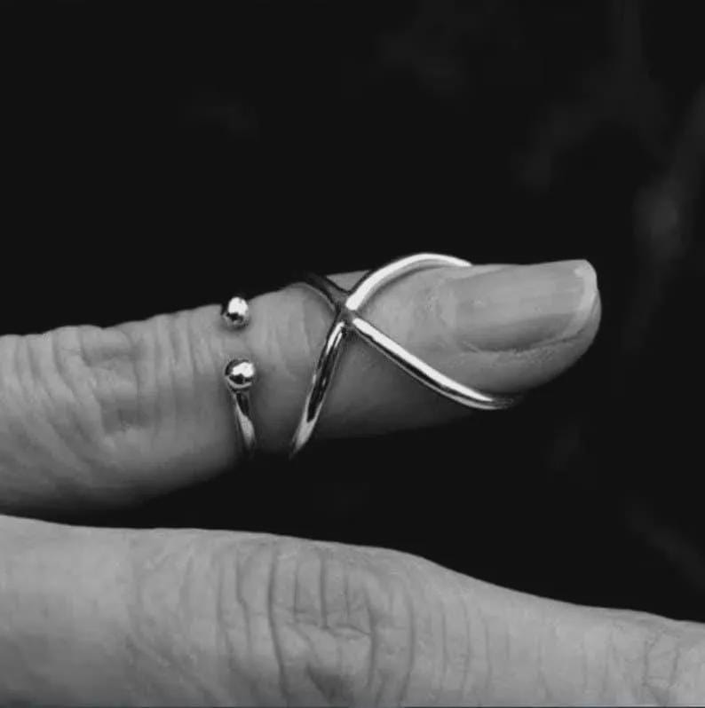 May include: A silver ring with an X-shaped design on the finger. A smaller ring with two silver spheres is also visible. The jewellery is set against a dark background.