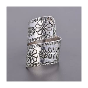 Könnte beinhalten: Silberring mit floralem Design. Der Ring ist breit und umschließt den Finger. Die Blumen sind geprägt und haben ein detailliertes Design.