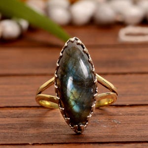 May include: A gold ring with a large, oval-shaped labradorite gemstone. The gemstone has a dark blue and green color with iridescent flashes.