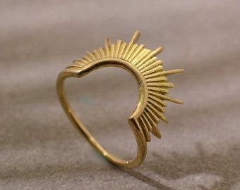 May include: A gold ring with a sunburst design. The ring is open in the back and has a pointed, heart-shaped opening.