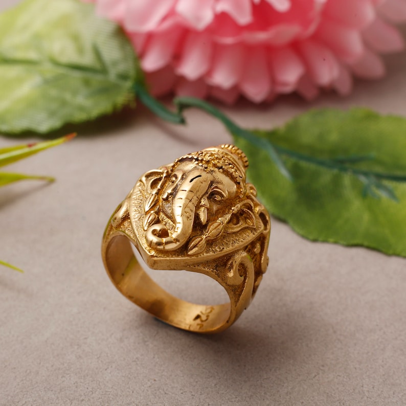 Puede incluir: Un anillo de color dorado con un dise&ntilde;o detallado de la deidad hind&uacute; Ganesha, un dios con cabeza de elefante, en el centro. El anillo est&aacute; hecho de metal y tiene una superficie texturizada.
