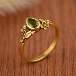 Op de afbeelding: Een gouden ring met een groene edelsteen en bloemmotieven.