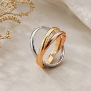 Può includere: Un anello tricolore composto da tre fasce intrecciate nei toni dell'argento, dell'oro giallo e dell'oro rosa. Le fasce metalliche lisce e arrotondate sono incastrate per creare una struttura circolare continua e stratificata con finitura lucida.