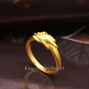 May include: A gold-colored ring with a floral design on the top. The ring has a smooth, polished finish and is set against a dark background. The text "KingsJewelryShopIN" is visible on the bottom of the image.