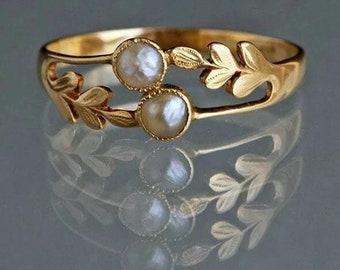 May include: A gold ring with two white pearl-like stones and a delicate leaf design.