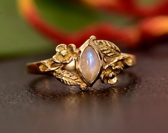 May include: A gold ring with a delicate floral design featuring a marquise-shaped moonstone.