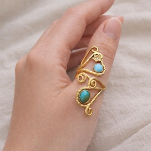 May include: A gold-colored ring with a floral design and two turquoise-colored stones. The ring has an open design that wraps around the finger. The ring is made of metal.