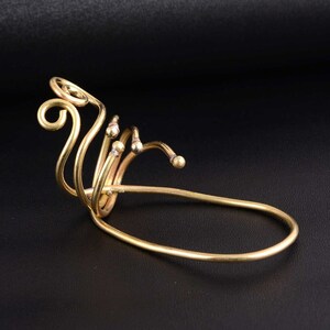 Puede incluir: Un brazalete de oreja dorado con un diseño en espiral y pequeñas cuentas. El brazalete está hecho de alambre y está diseñado para envolverse alrededor de la oreja.