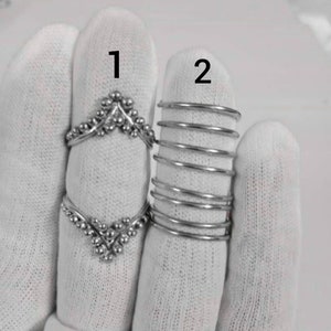 May include: Two silver rings on a white background. The ring labeled "1" is a delicate, open-ended ring with a V-shaped design. The ring labeled "2" is a stack of five thin silver bands.