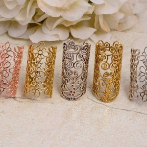 Può includere: Cinque anelli decorativi in metallo con intricati disegni floreali e a spirale. Gli anelli sono di diversi colori, tra cui oro, argento e oro rosa.