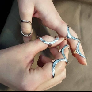 May include: A set of four silver rings designed to be worn on the fingers. The rings are made of a smooth, shiny metal and have a unique, abstract design.