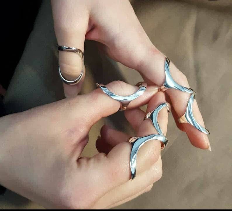 May include: A set of four silver rings designed to be worn on the fingers. The rings are made of a smooth, shiny metal and have a unique, abstract design.