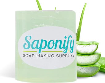 May include: A translucent, light green soap block with the text "Saponify SOAP MAKING SUPPLIES" on a white oval label. Fresh aloe vera leaves and slices are arranged near the soap, suggesting natural ingredients for soap making.