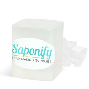 May include: A clear, rectangular block of soap with the word "Saponify" in teal script on a white oval label. The label also reads "SOAP MAKING SUPPLIES". Several smaller, clear soap pieces are to the right.