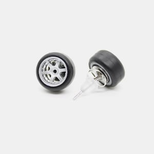 May include: A pair of silver and black tire stud earrings. The earrings are shaped like a tire with a silver rim and a black tire.
