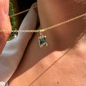 Puede incluir: Un collar de cadena de oro con un colgante de piedra preciosa verde. El colgante tiene forma rectangular con un corte facetado.
