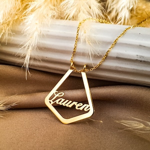 May include: Gold necklace with a geometric pendant featuring the name "Lauren" cut out.