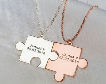 May include: Two silver necklaces with matching puzzle piece pendants. The pendant on the left is silver and says "Jannet ♥ 08.03.2018". The pendant on the right is rose gold and says "James ♥ 08.03.2018".