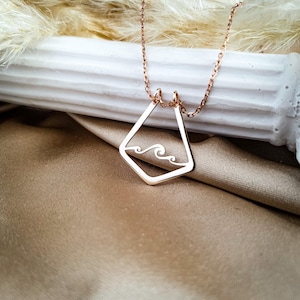 K&ouml;nnte beinhalten: Eine Halskette aus Ros&eacute;gold mit einem geometrischen Anh&auml;nger, der ein Wellenmuster zeigt. Der Anh&auml;nger hat eine Diamantform mit einer ausgeschnittenen Welle im Inneren.