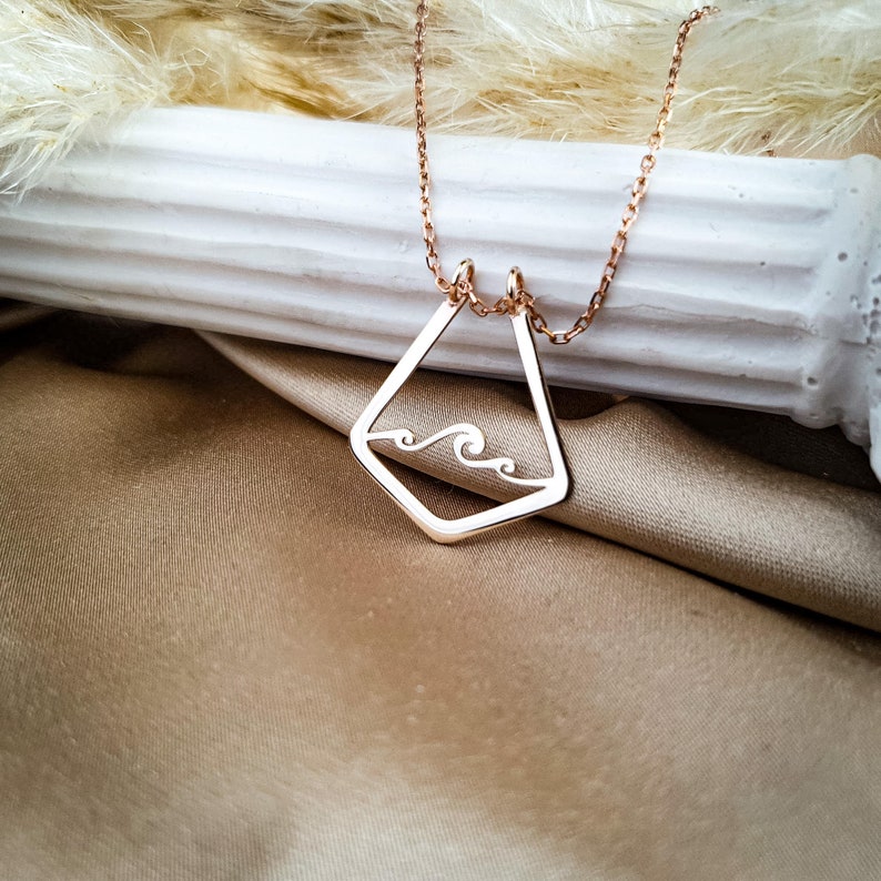 K&ouml;nnte beinhalten: Eine Halskette aus Ros&eacute;gold mit einem geometrischen Anh&auml;nger, der ein Wellenmuster zeigt. Der Anh&auml;nger hat eine Diamantform mit einer ausgeschnittenen Welle im Inneren.