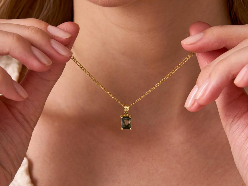 May include: A gold chain necklace with a dark green gemstone pendant. The pendant is a rectangular emerald cut.