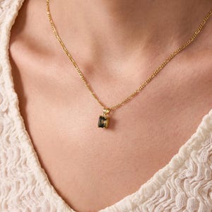 May include: A gold chain necklace with a small, square-shaped pendant featuring a dark green gemstone.