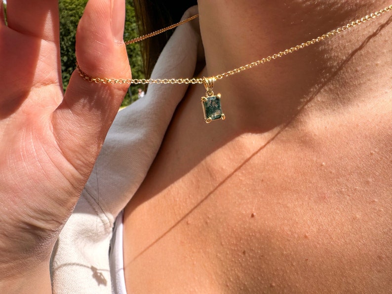 May include: A gold chain necklace with a green gemstone pendant. The pendant is a rectangular shape with a faceted cut.