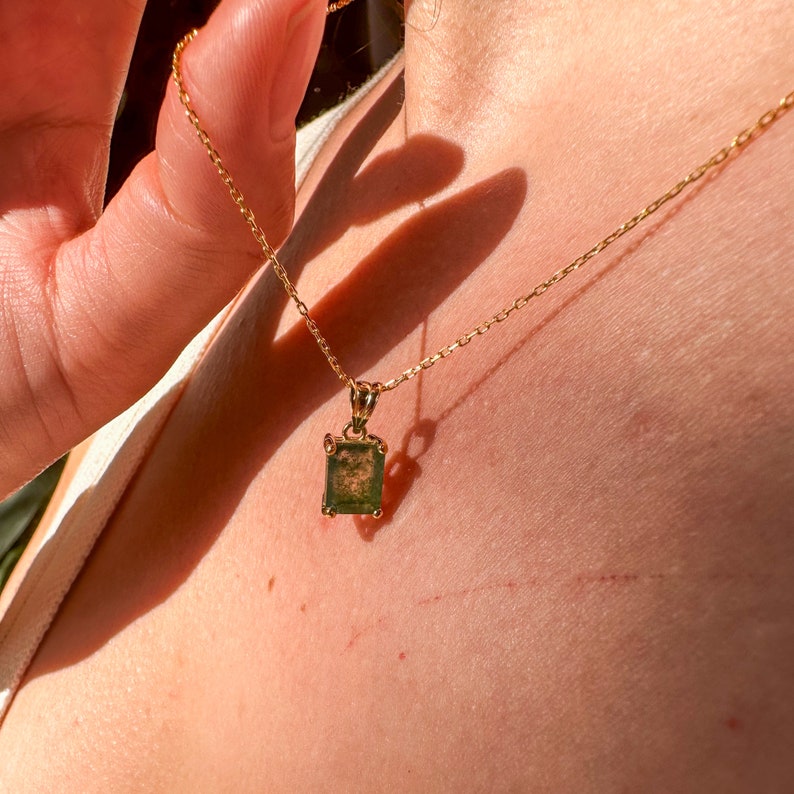 May include: A gold chain necklace with a square green gemstone pendant.