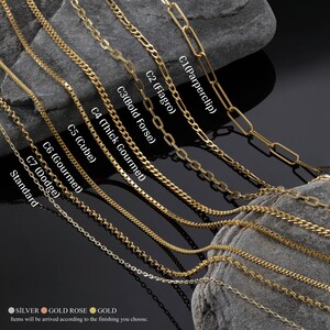 K&ouml;nnte beinhalten: Nahaufnahme von zehn verschiedenen Goldketten-Stilen, darunter eine Paperclip-Kette, eine Figaro-Kette, eine Bold-Forsey-Kette, eine Thick-Gourmet-Kette, eine Cube-Kette, eine Gourmet-Kette, eine Dodge-Kette und eine Standardkette. Die Ketten sind in einer Reihe auf einer grauen Steinoberfl&auml;che angeordnet.
