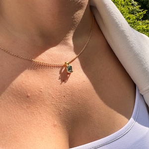 May include: A gold chain necklace with a small, square-shaped pendant featuring a dark green gemstone.