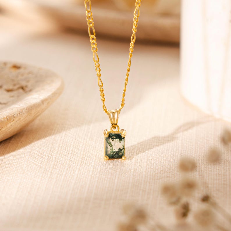 May include: A gold chain necklace with a green and white agate stone pendant. The pendant is a rectangular shape with a gold frame.