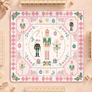 May include: A square board game featuring a central illustration of a nutcracker, a mouse in a uniform, and a ballerina surrounded by holiday icons. The border has a pink and white diamond pattern with nutcracker figures and ornaments.