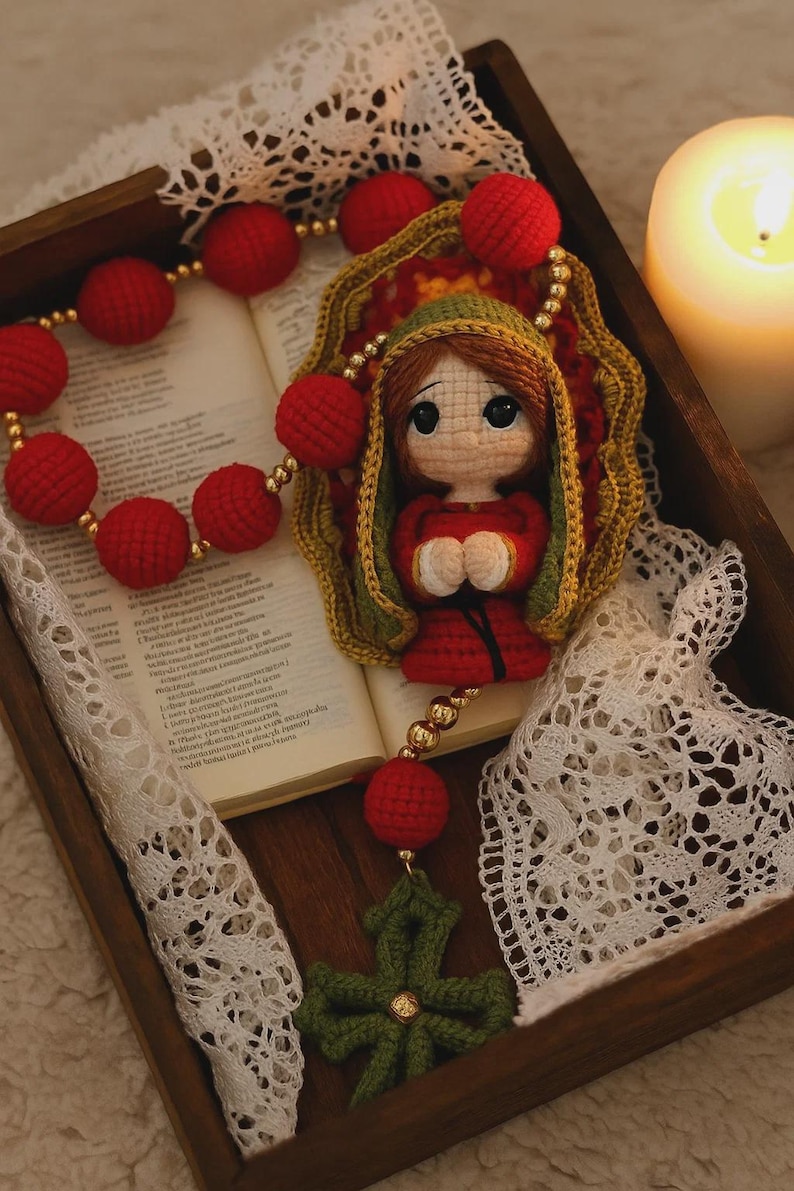 Puede incluir: Un rosario hecho a mano con cuentas rojas y una cruz verde. La pieza central presenta una figura de mu&ntilde;eca con una t&uacute;nica roja y un chal verde. El rosario se exhibe en una bandeja de madera con un libro y una vela encendida.